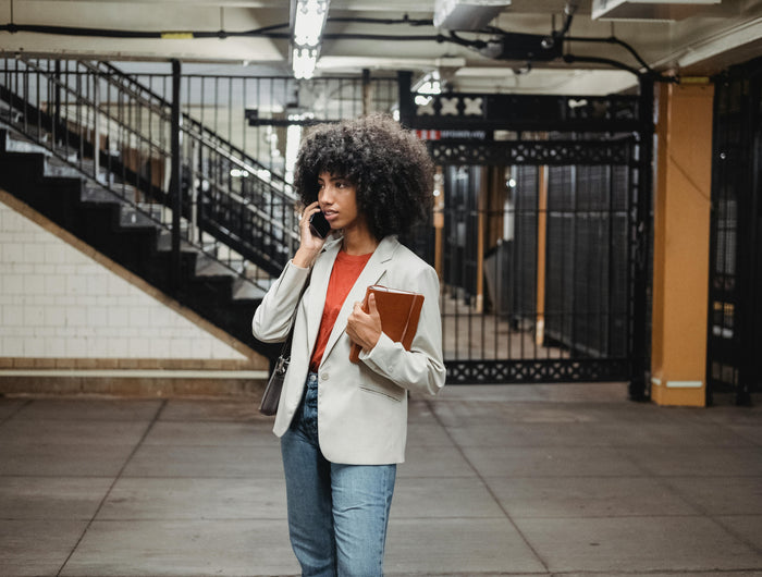 Young professional woman holding a notebook while on the phone at the subway platform — daily planning on the go