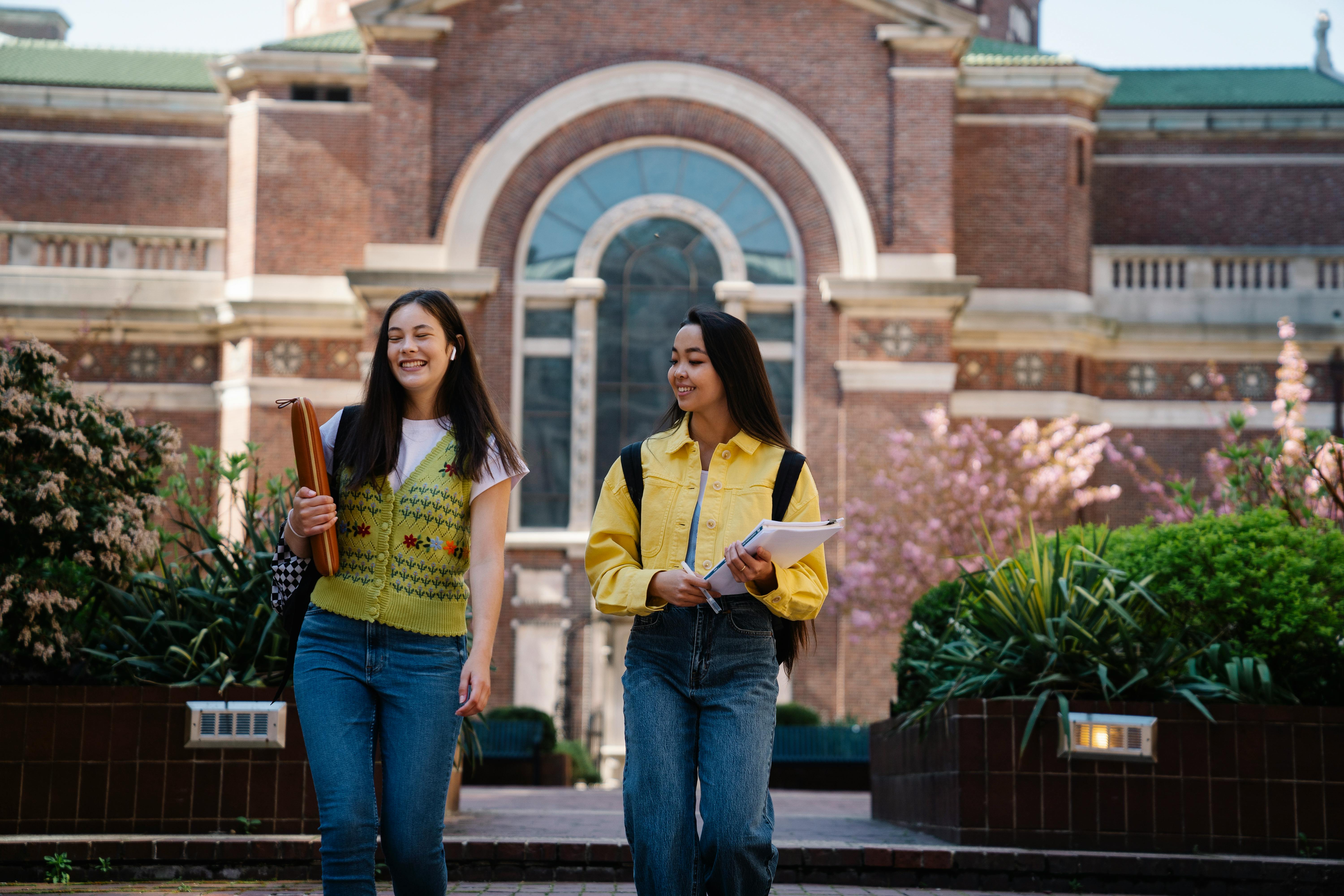 Two university students walking on campus holding memo notepads and planning tools, representing organized student life